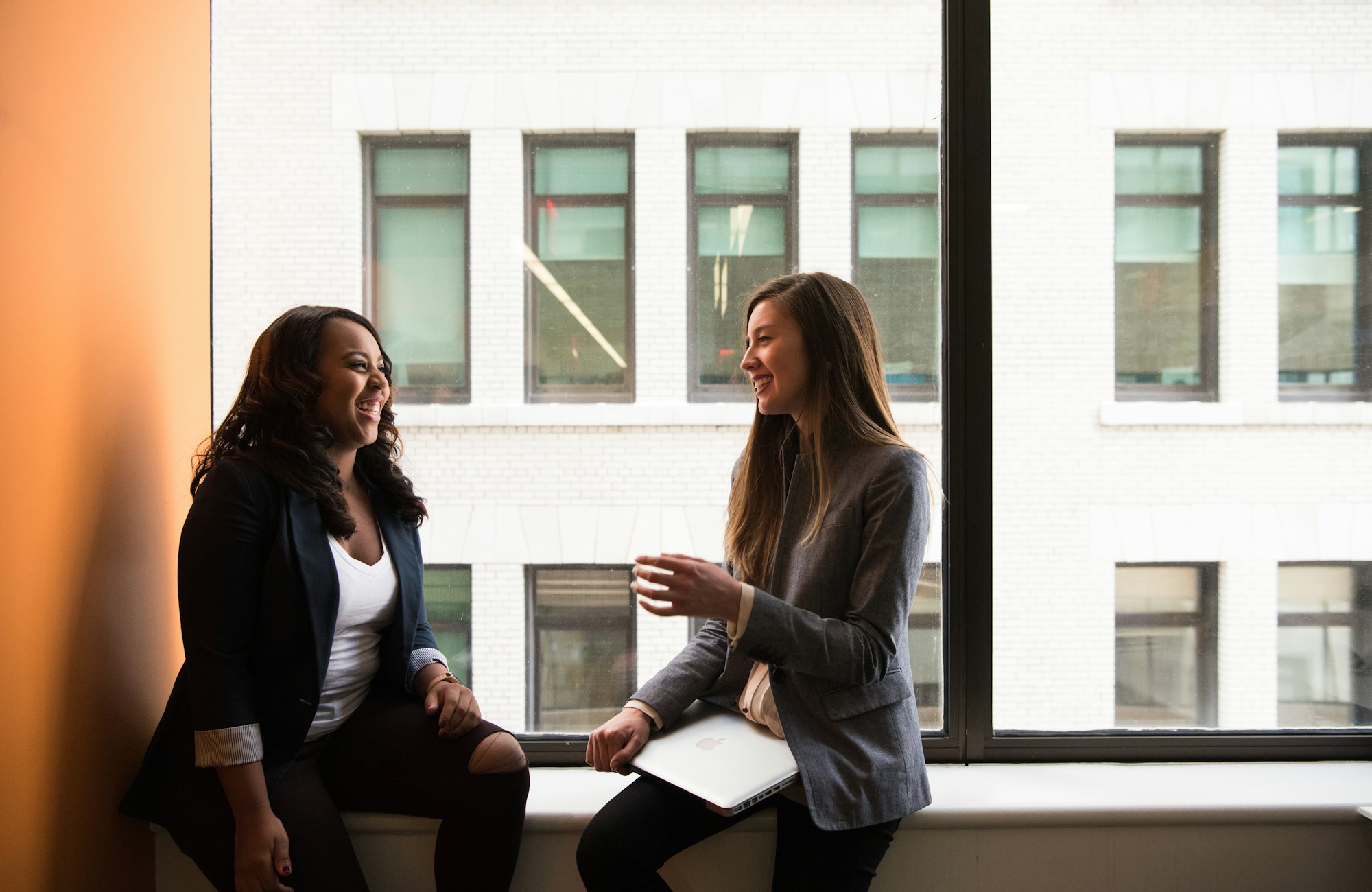 Two colleagues talking and laughing on a window ledge